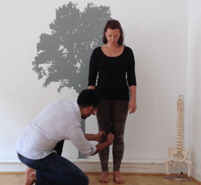 Posture Specialist examining a woman's knee position while she stands in a posture clinic