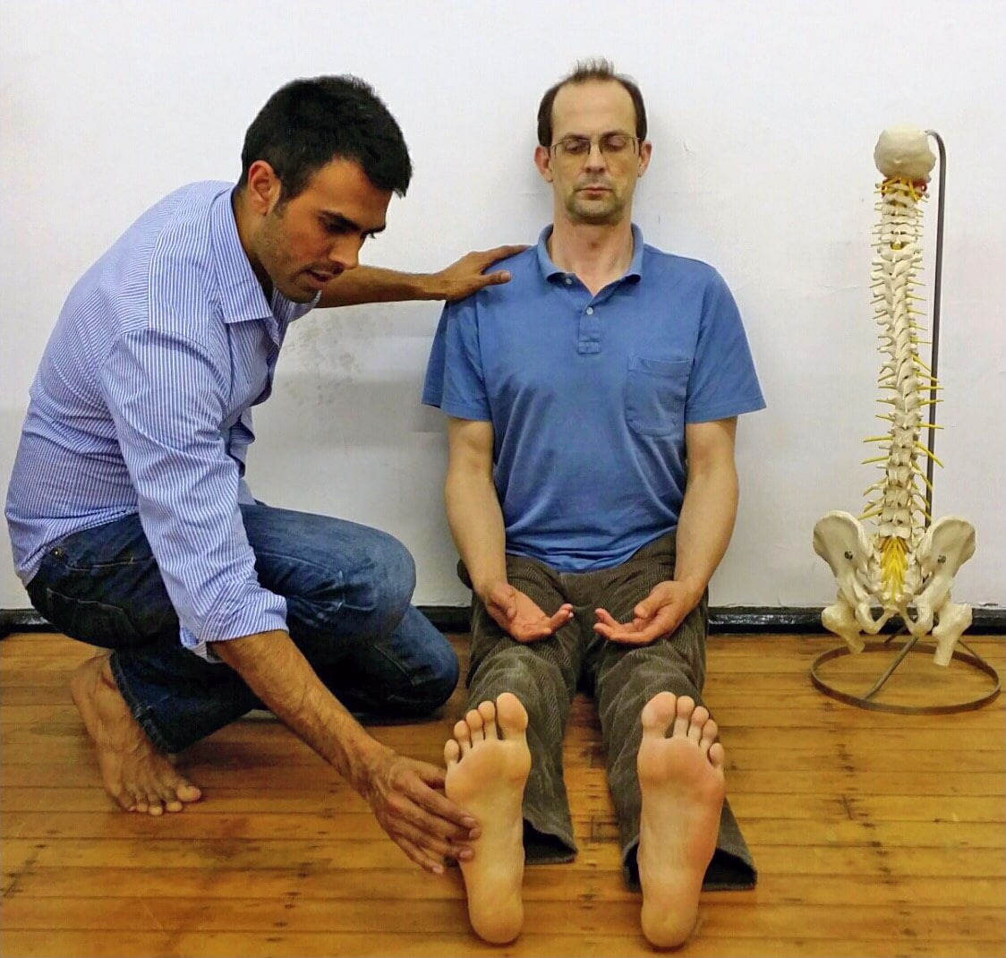 Posture Specialist adjusting a client's foot while doing a posture exercise sitting against the wall