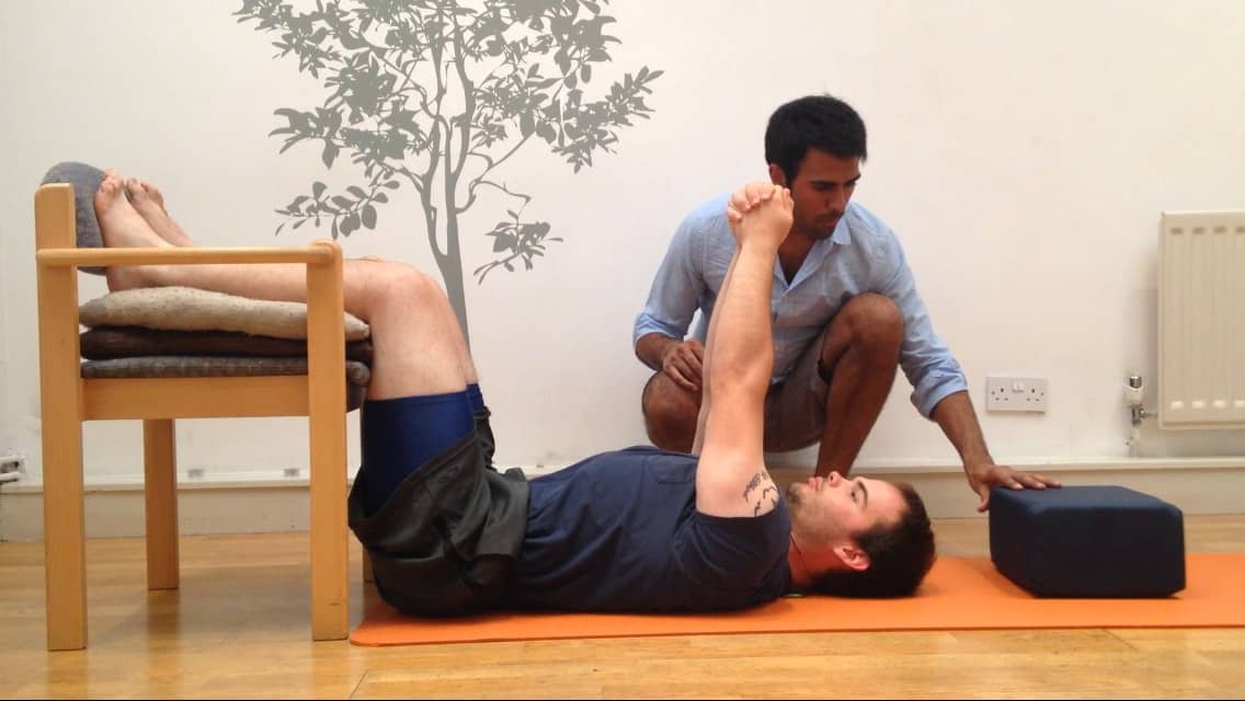 Posture Specialist helping a patient perform a posture correction exercise on the floor with his legs on a chair
