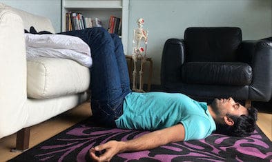 Man doing a posture correction exercise lying down on the floor with legs on a sofa