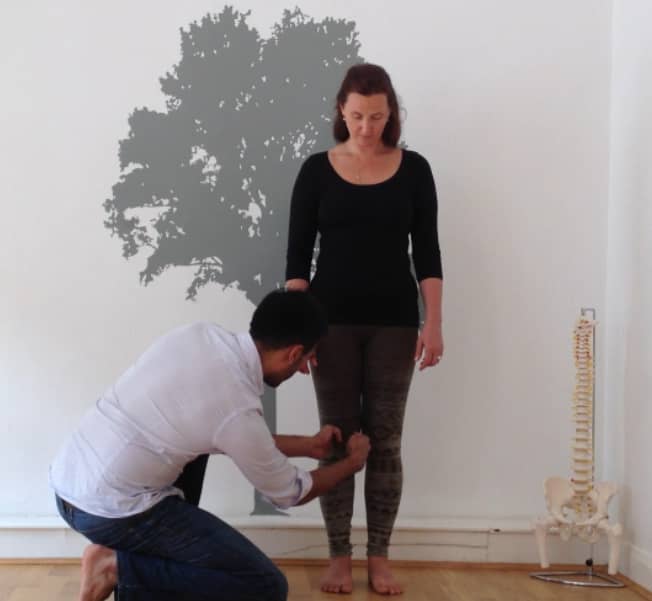 Posture Specialist examining alignment of a woman's knee while she stands